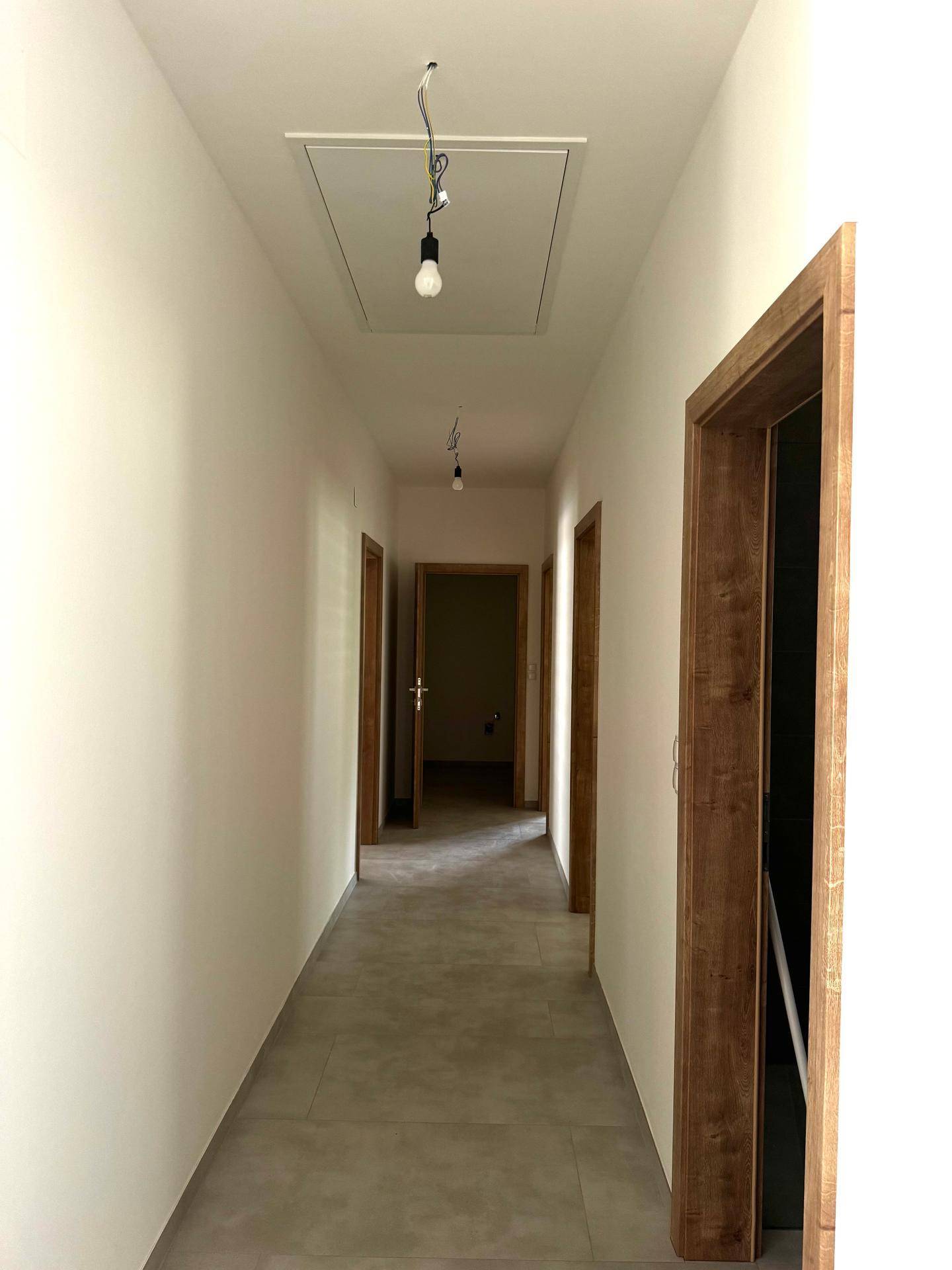 Heller Flur mit grauen Fliesen und mehreren Holztüren, der zu den verschiedenen Räumen führt.