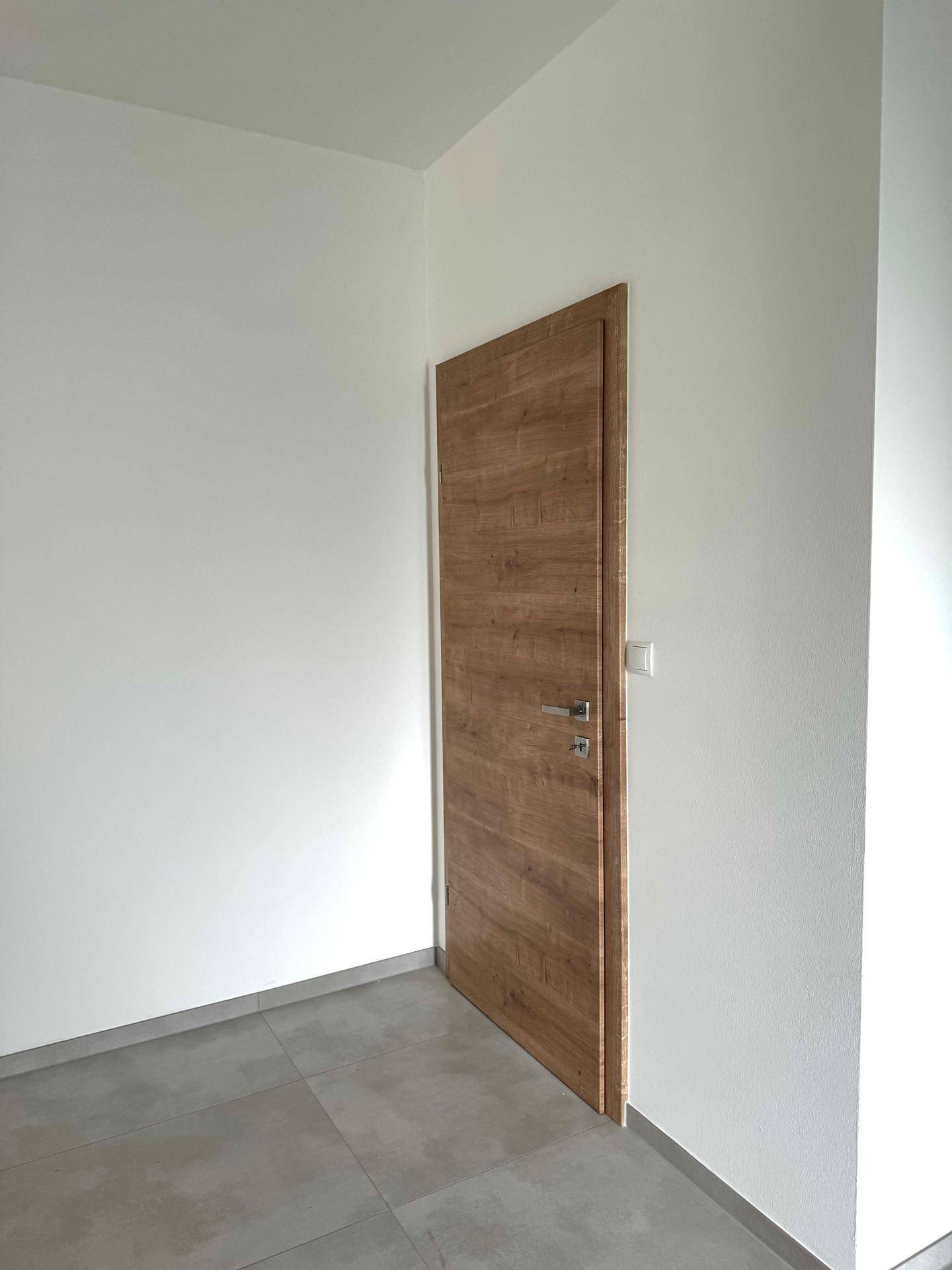 Heller Innenraum mit einer modernen Holztür und grauen Fliesen, bereit für die Einrichtung.