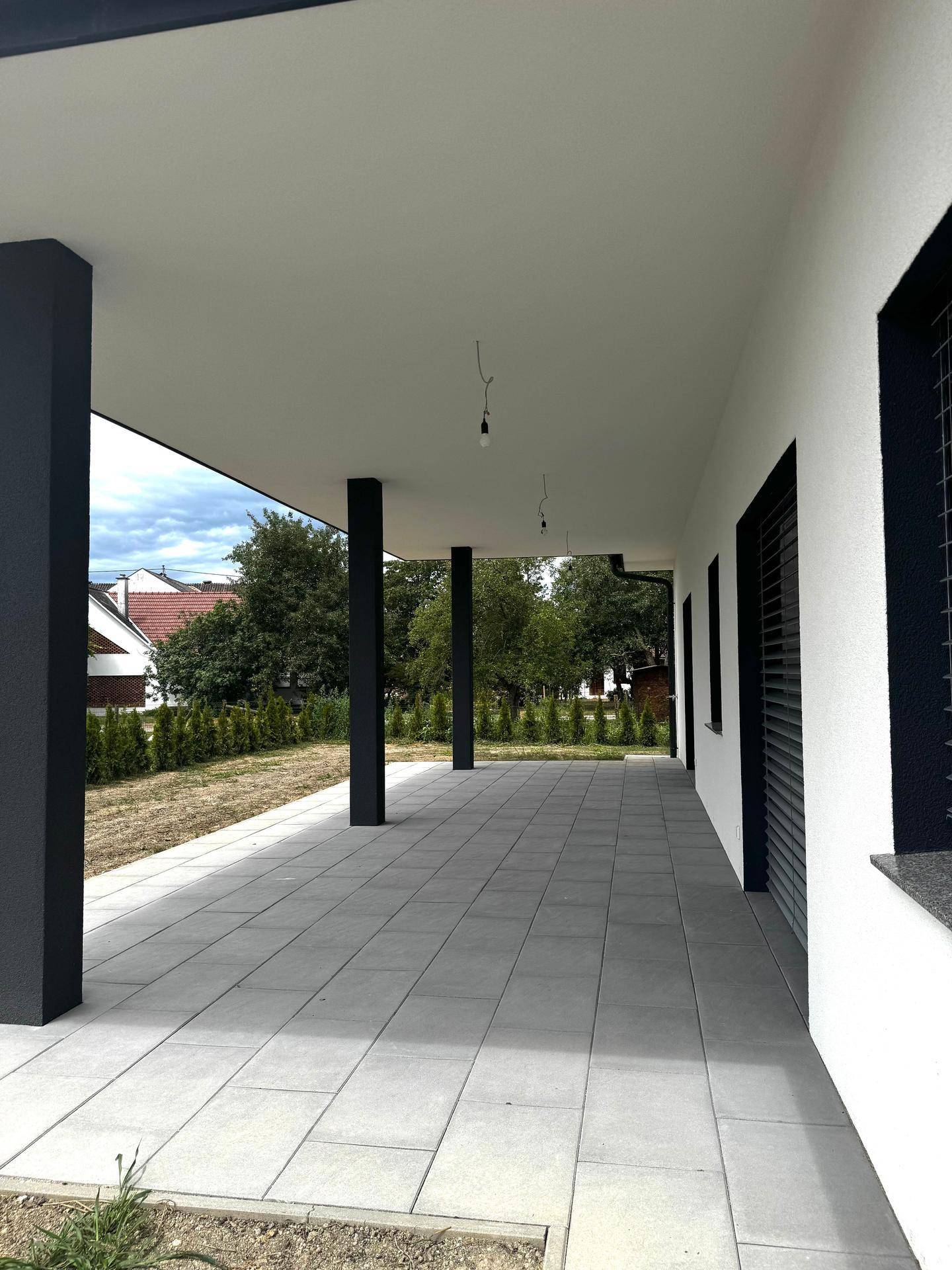 Überdachte Terrasse mit grauen Fliesen und dunklen Säulen, ideal für entspannte Stunden im Freien.