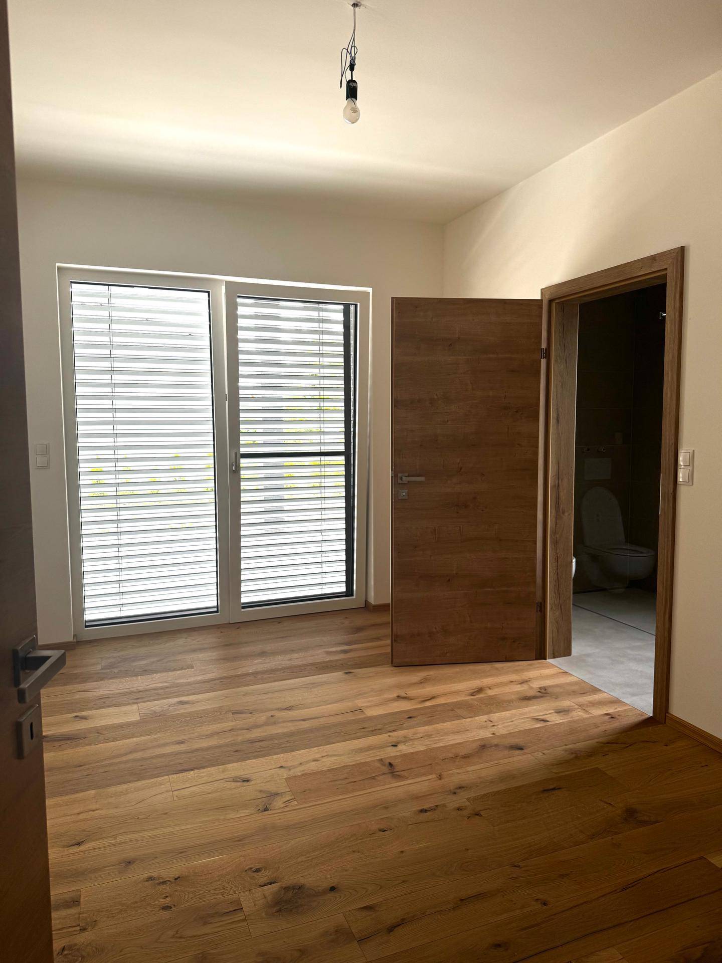 Geräumiges Schlafzimmer mit Holzboden, großen Fenstern und direktem Zugang zum Badezimmer.