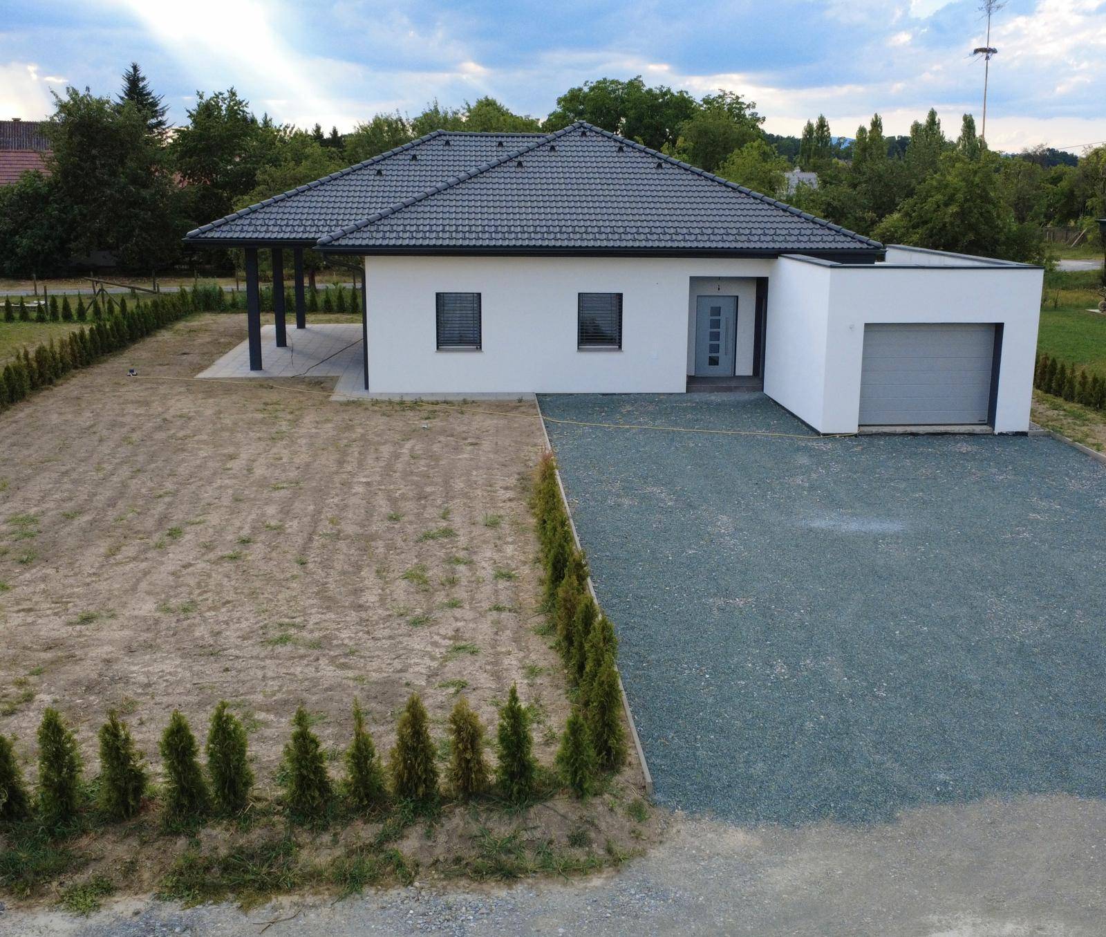 Neubau-Einfamilienhaus mit dunklem Dach, integrierter Garage und unfertigem Gartenbereich.