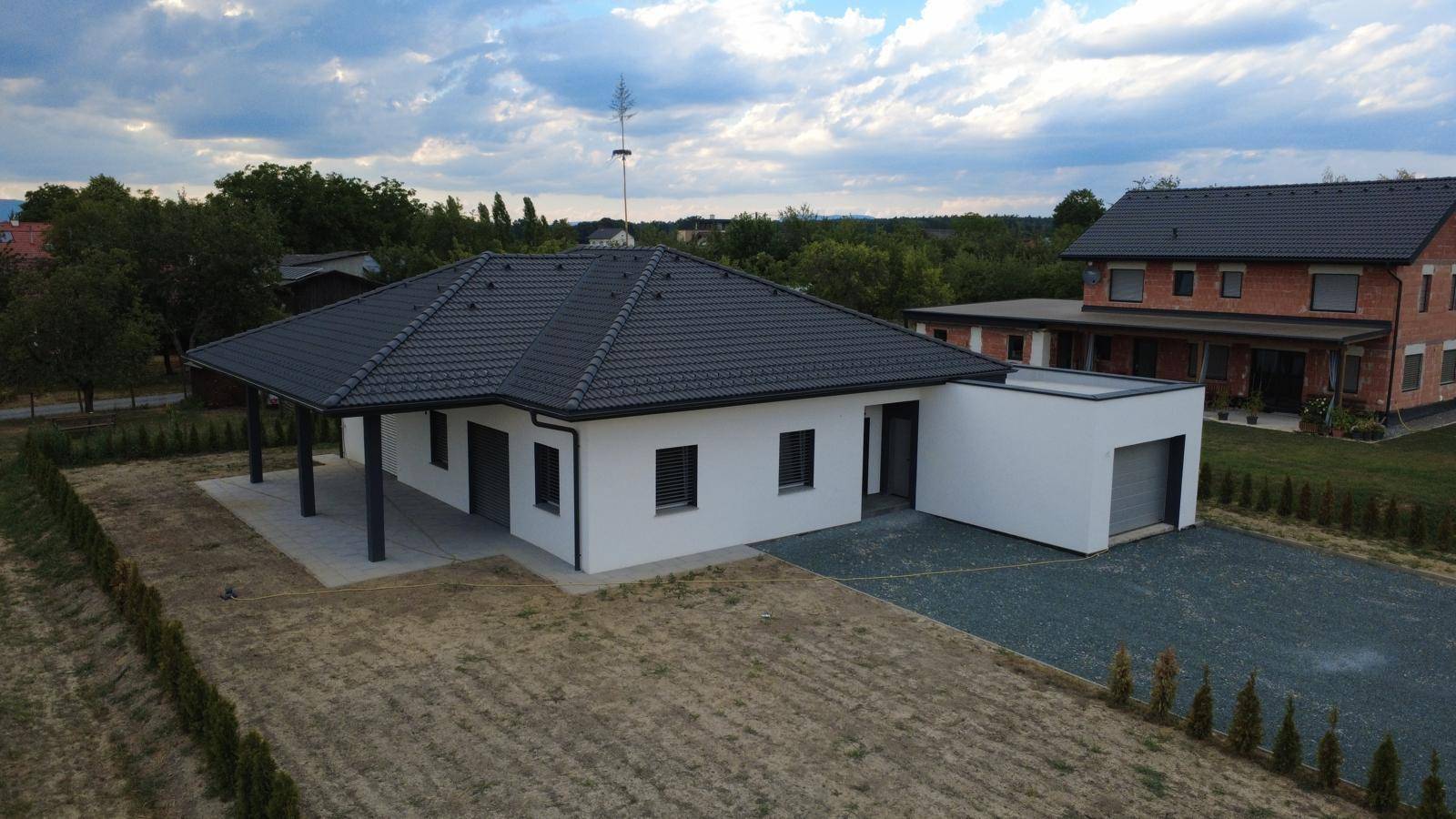 Modernes Einfamilienhaus mit dunklem Ziegeldach und angrenzender Garage in ländlicher Umgebung.