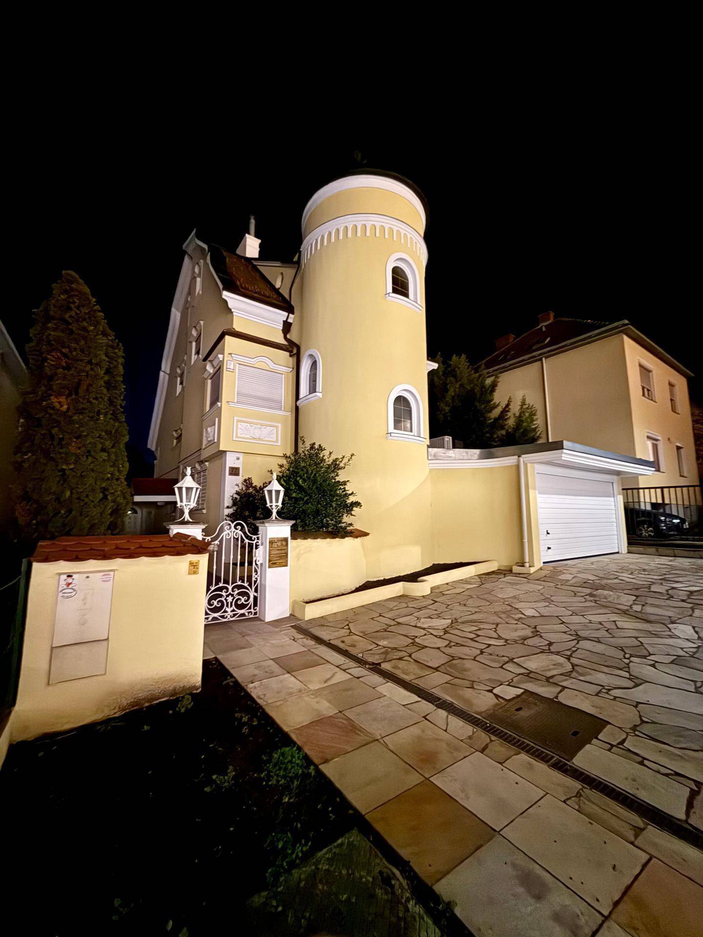 Elegante Stadtvilla bei Nacht mit markantem Turm, verzierter Toreinfahrt und integrierter Garage.