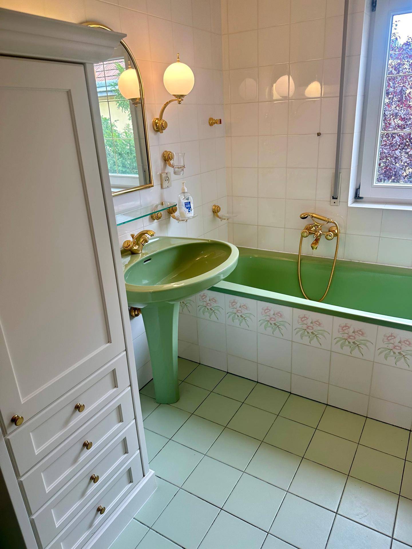 Badezimmer im 80er-Jahre-Stil mit grüner Badewanne, passendem Waschbecken und Fenster.