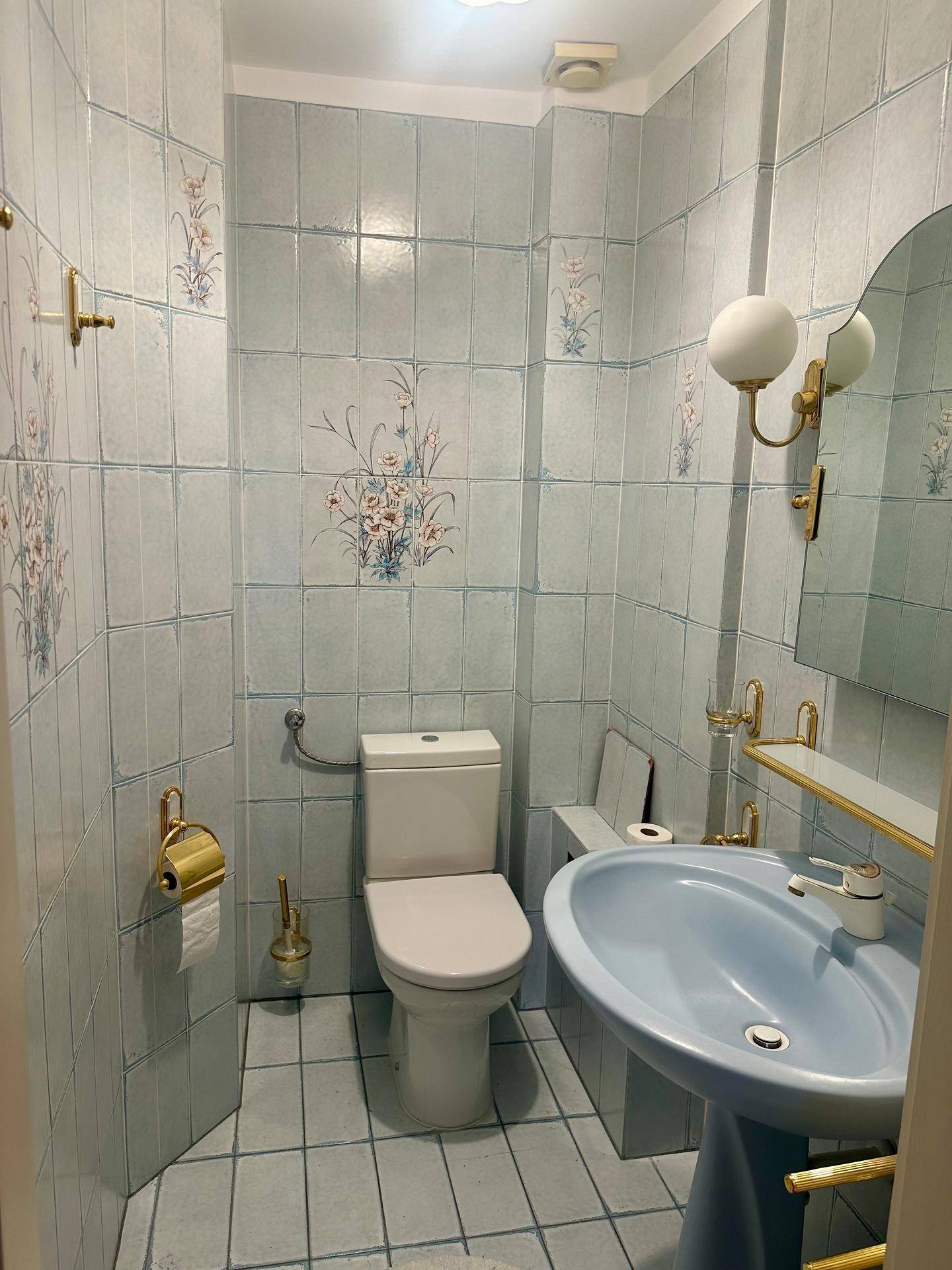 Kleines Gäste-WC mit blauen Fliesen, floralen Mustern und passendem Waschbecken.