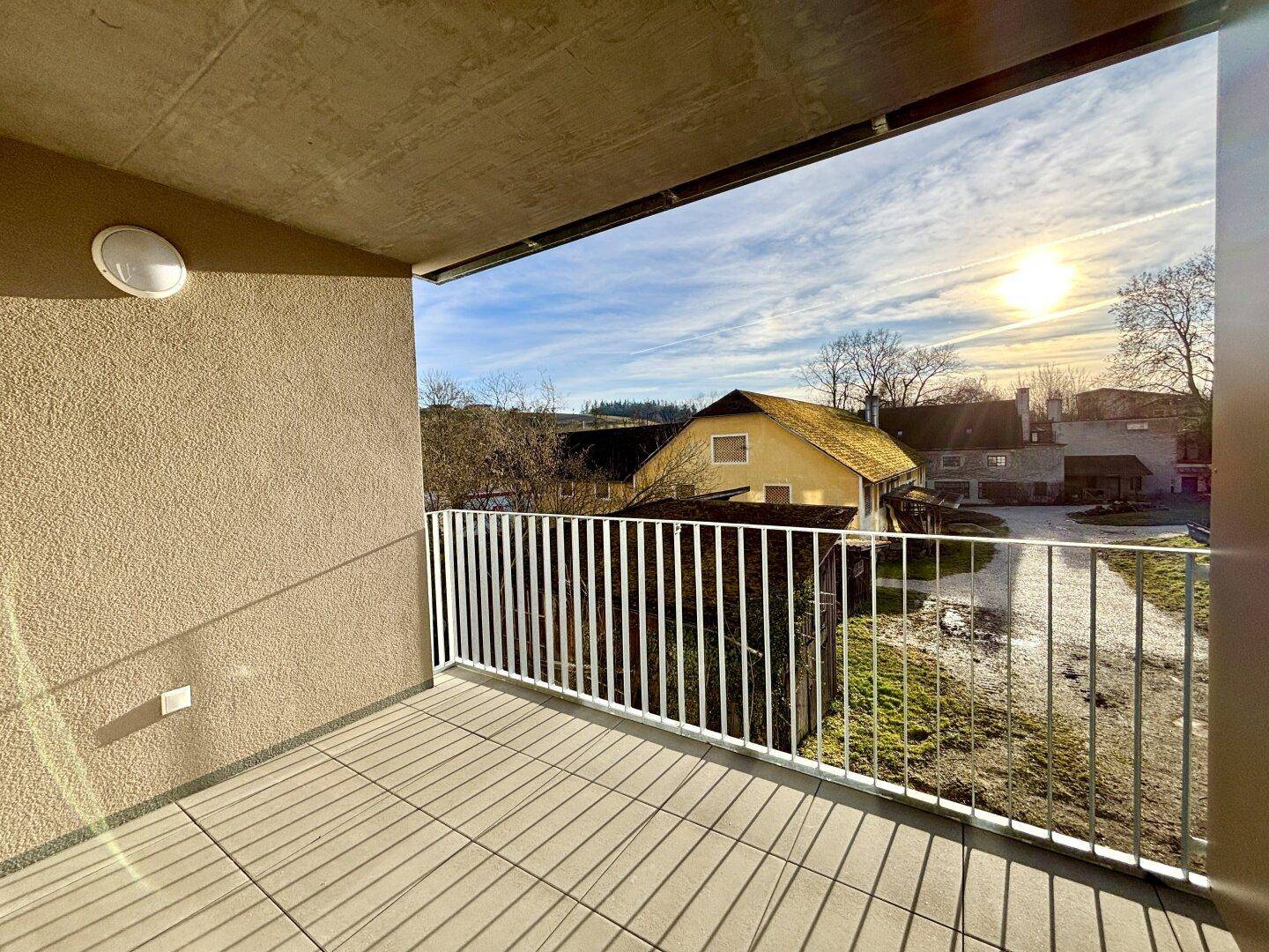 Sonniger Balkon mit Blick auf die grüne Umgebung und ländliche Häuser im Hintergrund.