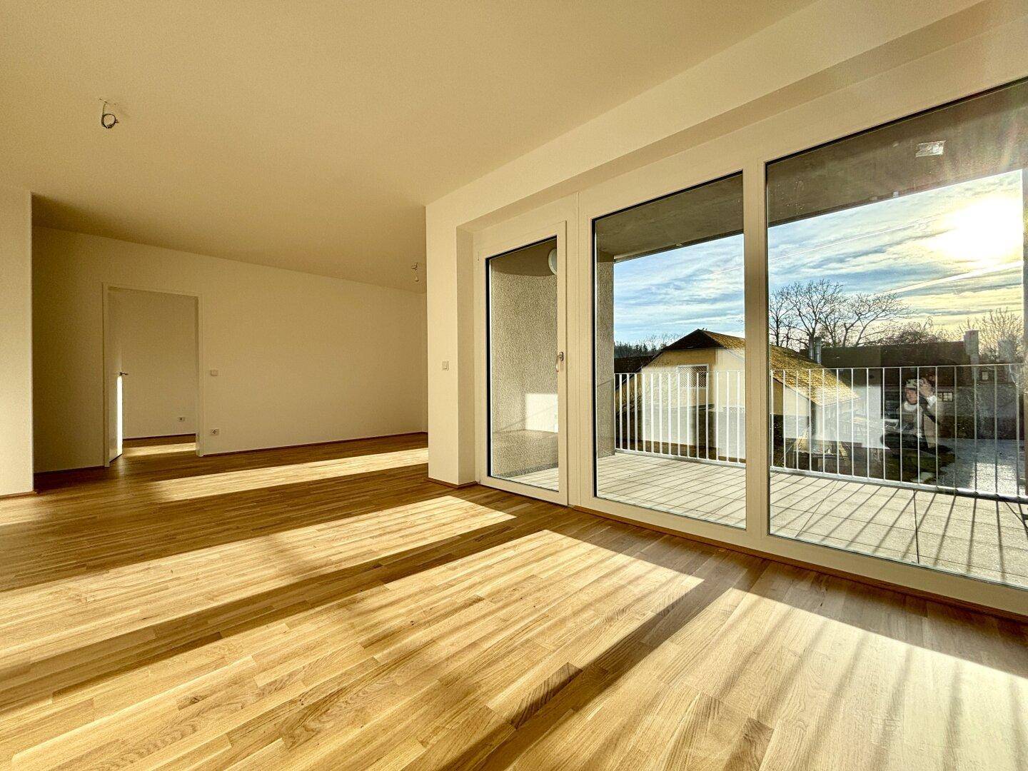 Helles Wohnzimmer mit Holzboden und Zugang zu einem sonnigen Balkon, ideal für Neubauwohnungen.