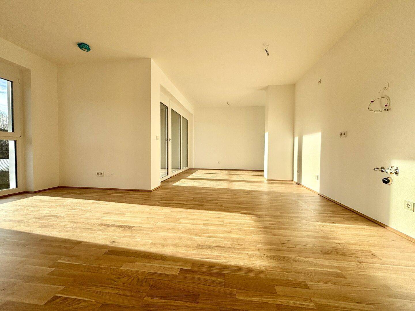 Helles, leeres Zimmer mit Parkettboden und großen Fenstern, das viel natürliches Licht hereinlässt.