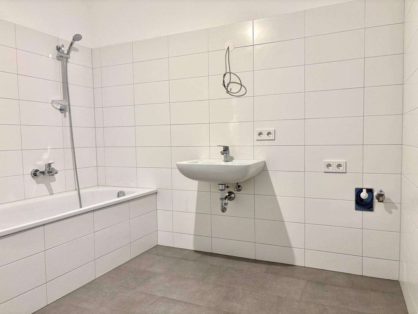Modern gefliestes Badezimmer mit Badewanne, Dusche und Waschbecken, noch ohne Armaturen.