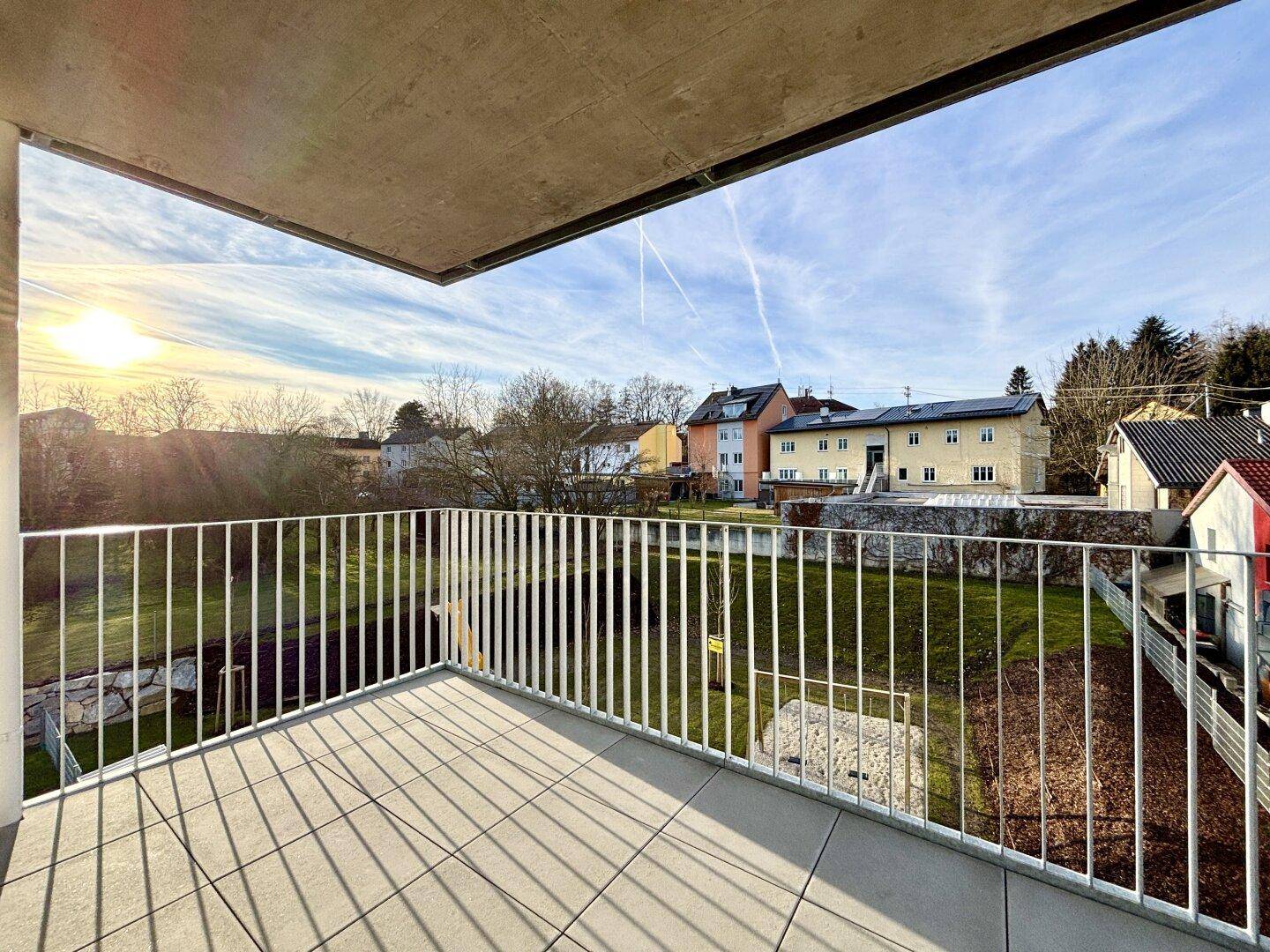Helles Balkon mit Fliesenboden und Blick auf die umliegende Wohngegend bei Sonnenuntergang.