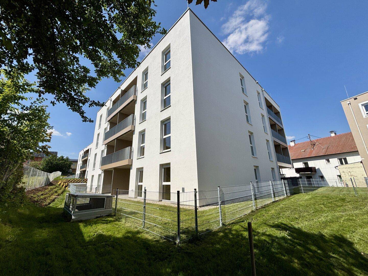 Moderne Architektur eines Neubaus mit weißer Fassade und mehreren Balkonen, umgeben von Grünflächen.