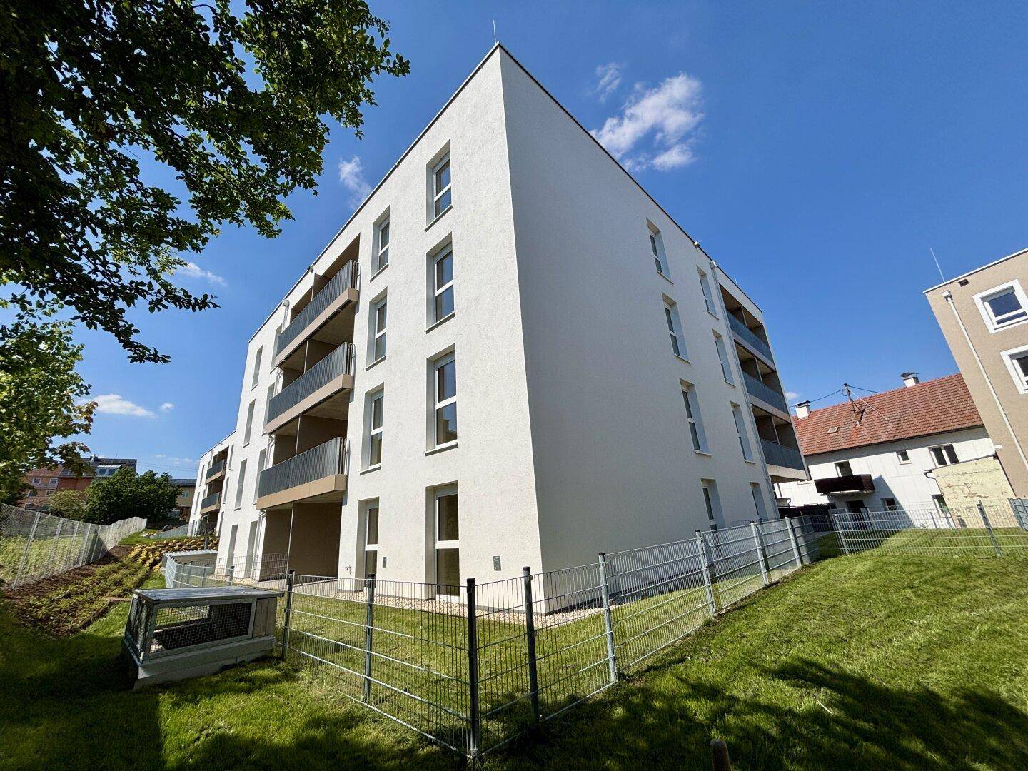 Modernes Mehrfamilienhaus mit weißer Fassade und Balkonen unter blauem Himmel.