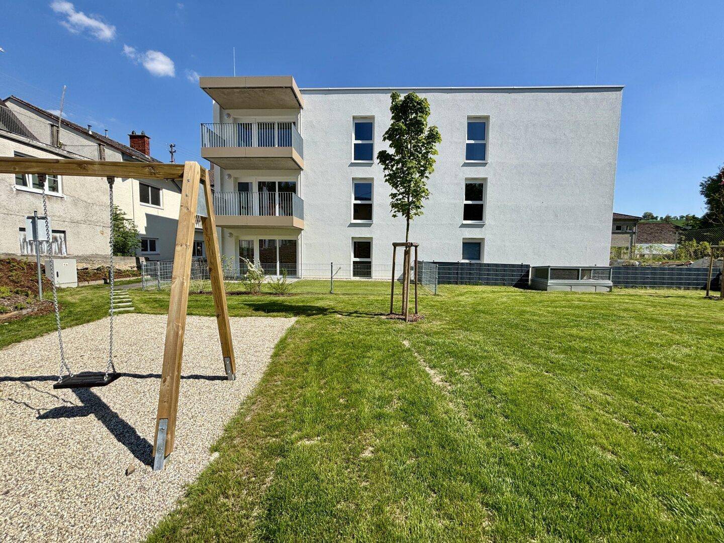 Moderne Wohnanlage mit Balkonen und einem sonnigen Spielplatz im Vordergrund.
