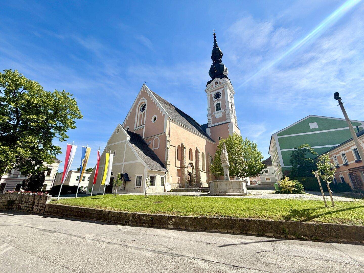 Historische Kirche mit Glockenturm, umgeben von bunten Flaggen und einem Brunnen.