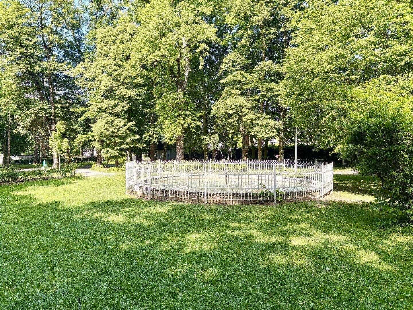 Eine kreisförmige, eingezäunte Fläche auf einer grünen Wiese, umgeben von Bäumen.