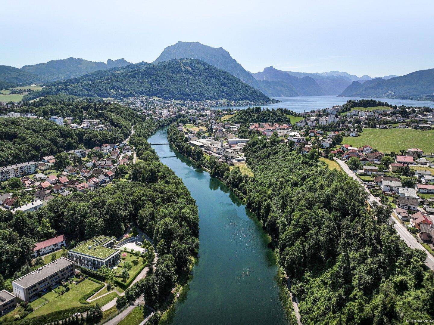 Luftaufnahme einer Stadt am Fluss mit See- und Bergblick in der Ferne.