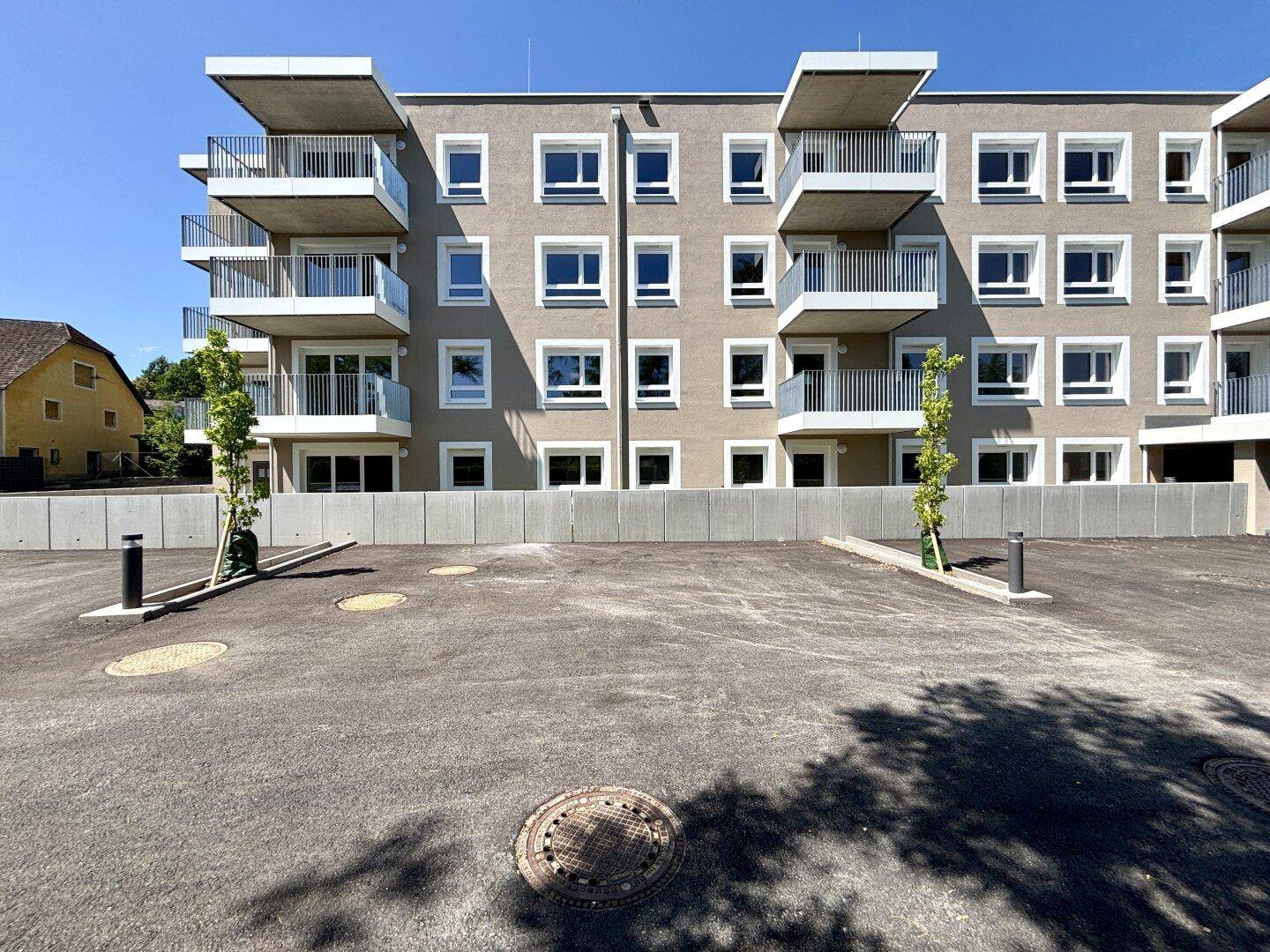Moderne Wohnanlage mit mehreren Balkonen und einem großzügigen Außenparkplatzbereich bei Sonnenschein.