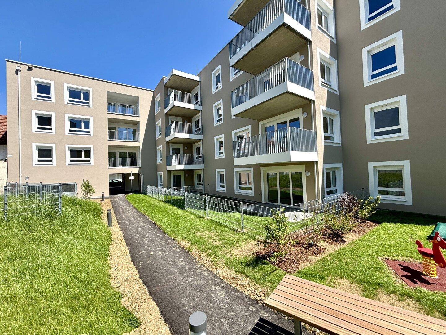 Neubau-Wohngebäude mit modernen Balkonen und gepflegten Grünflächen in sonniger Lage.