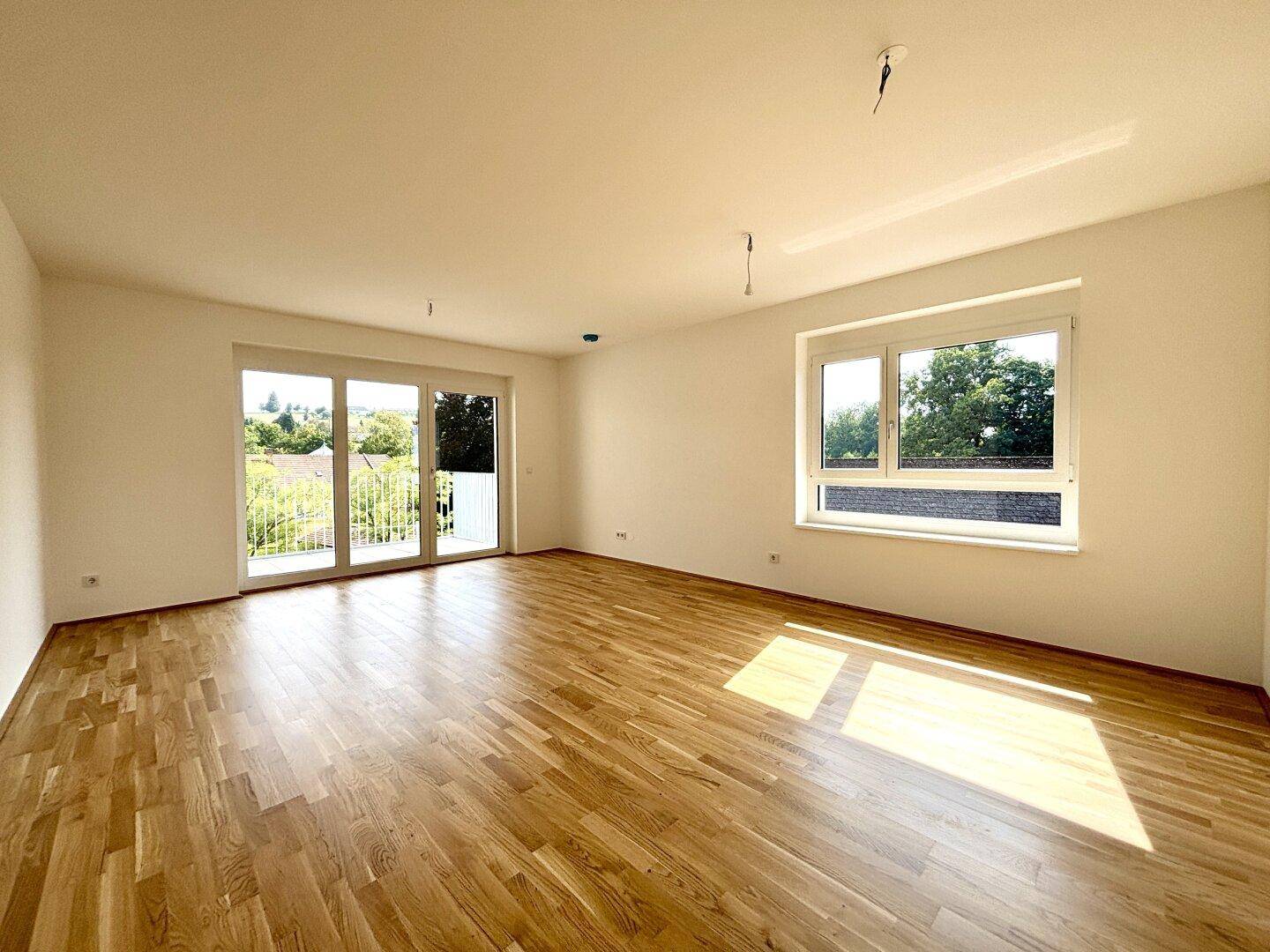 Helles, leeres Wohnzimmer mit Holzboden und Zugang zu einem Balkon.