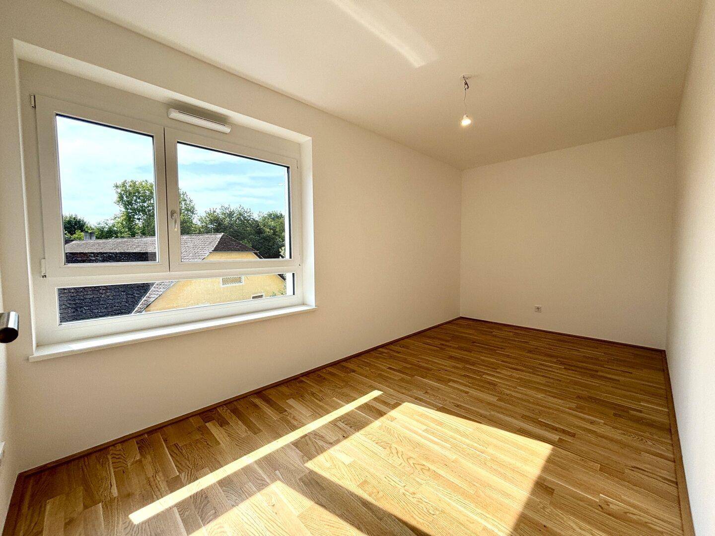 Heller Raum mit neuem Parkettboden und einem Fenster mit Blick auf die Nachbarschaft und Bäume.