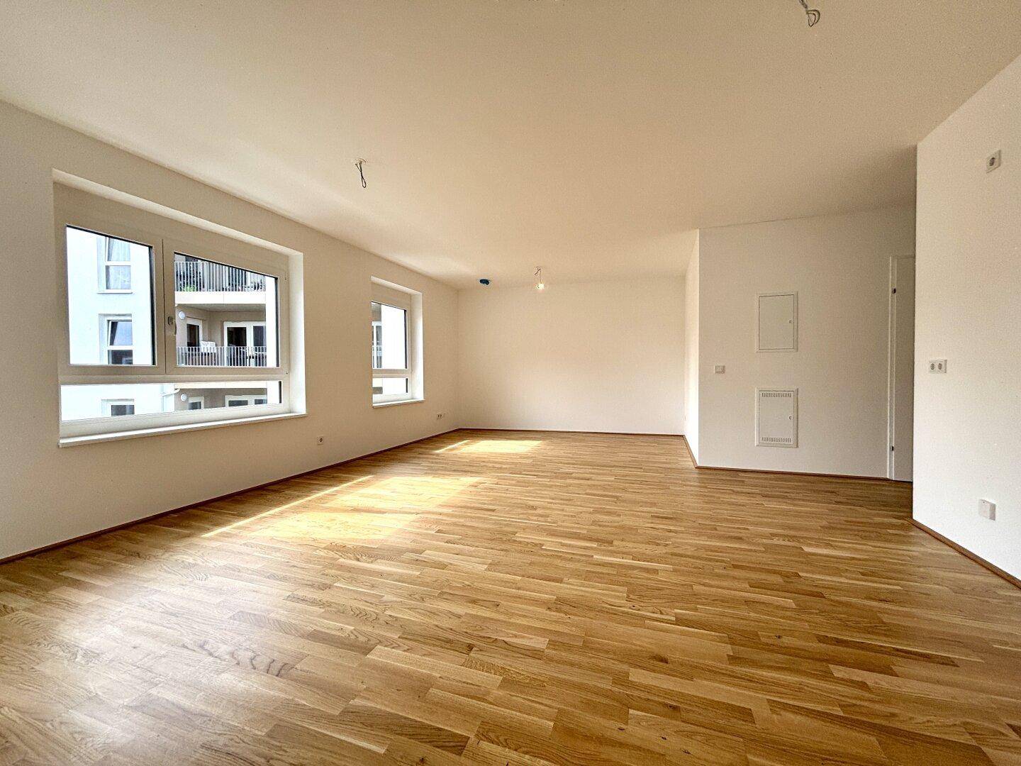 Geräumiges, helles Wohnzimmer mit hochwertigem Parkettboden und großen Fenstern.