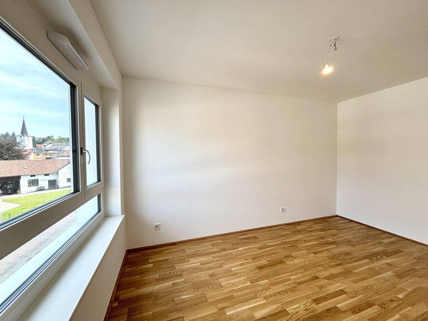 Helles Zimmer mit Parkettboden und weitem Blick auf die Umgebung durch große Fenster.