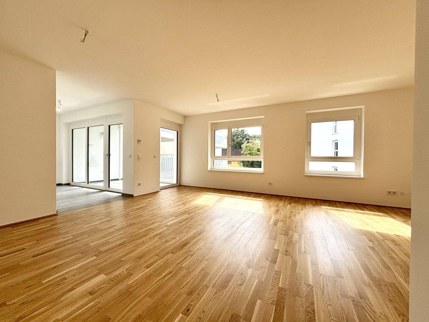 Lichtdurchfluteter Wohnbereich mit Eichenparkett und Zugang zum Balkon durch große Glasfronten.