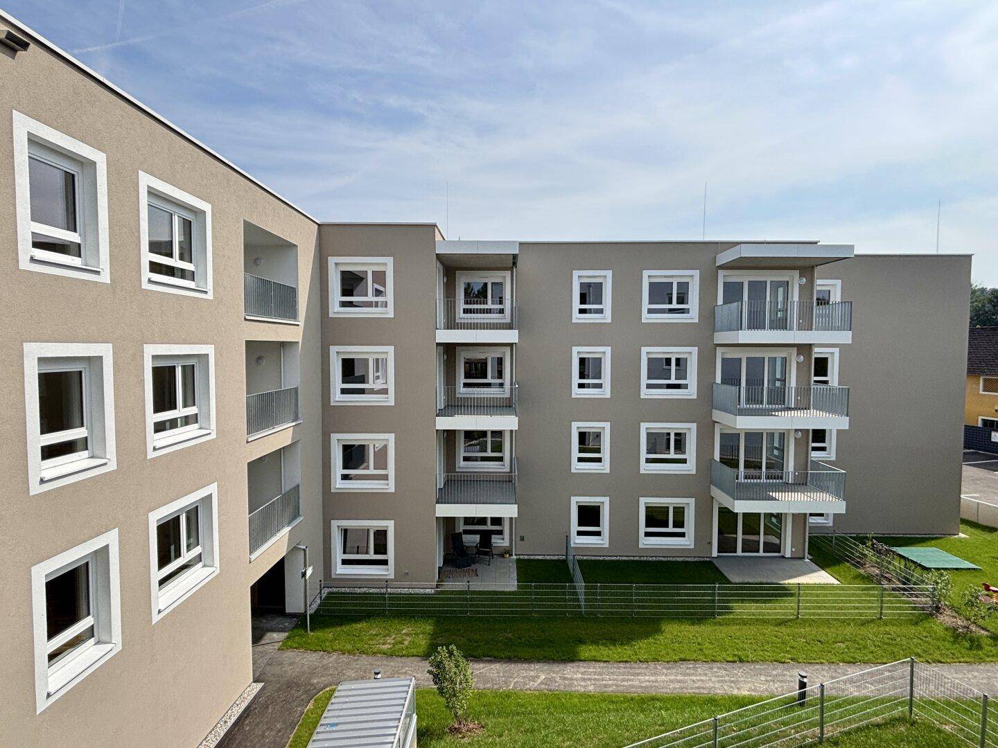 Gepflegte Grünfläche mit Rasen und einem Spielbereich neben dem modernen Wohngebäude.