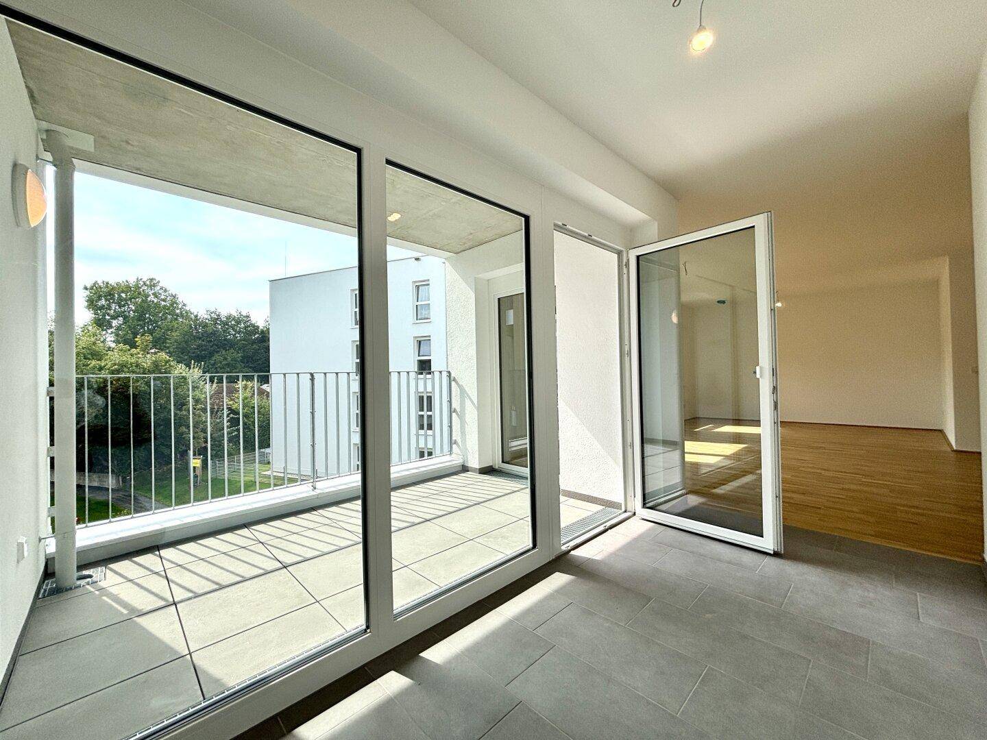Heller Balkon mit Fliesenboden und großen Glasfronten, die viel Tageslicht hereinlassen.