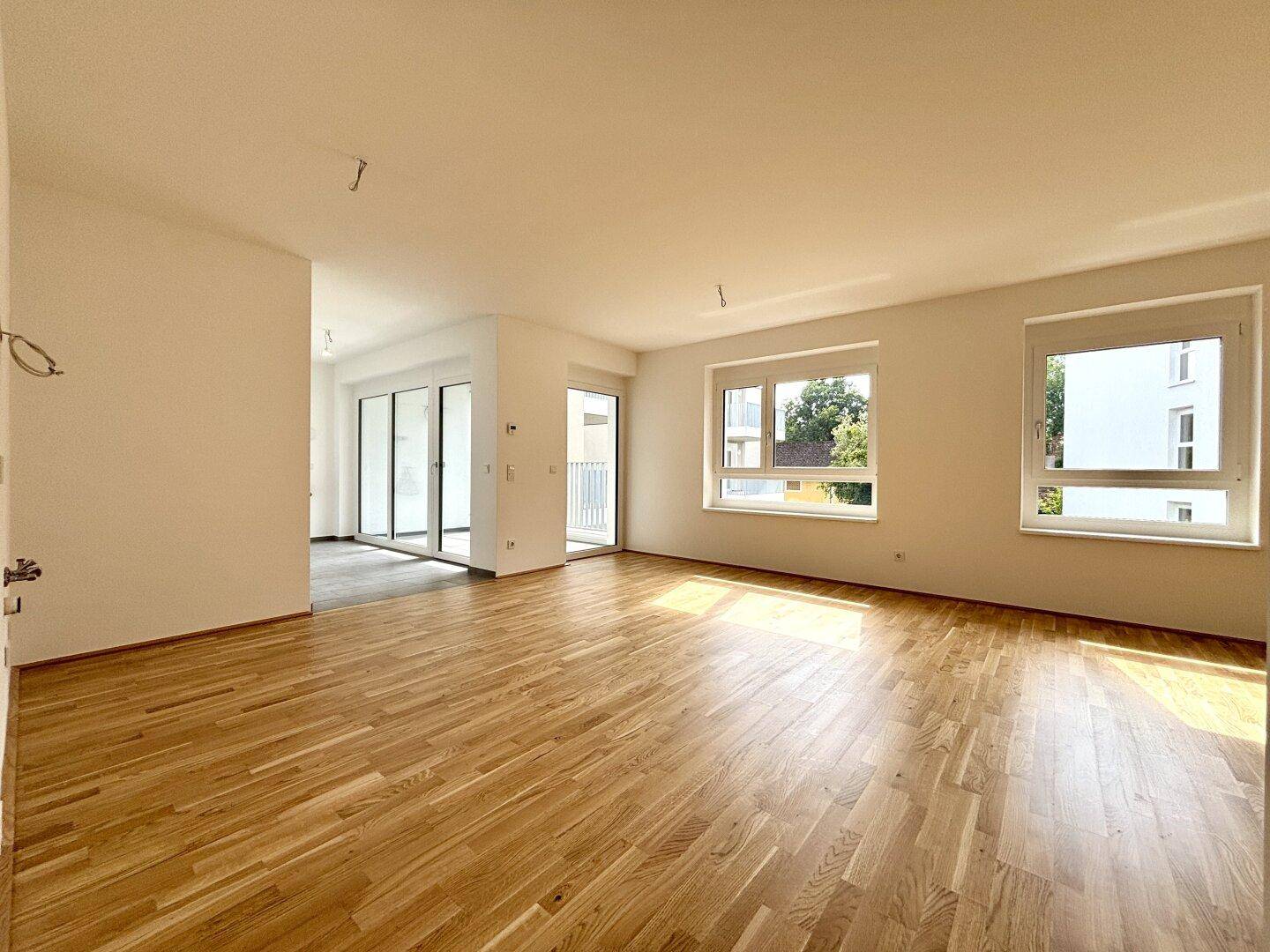Geräumiges, helles Wohnzimmer mit Parkettboden und Zugang zu einem Balkon.