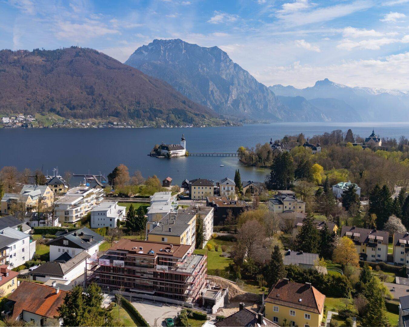 Luftaufnahme einer malerischen Stadt am Seeufer mit Bergen im Hintergrund und einer Inselburg.