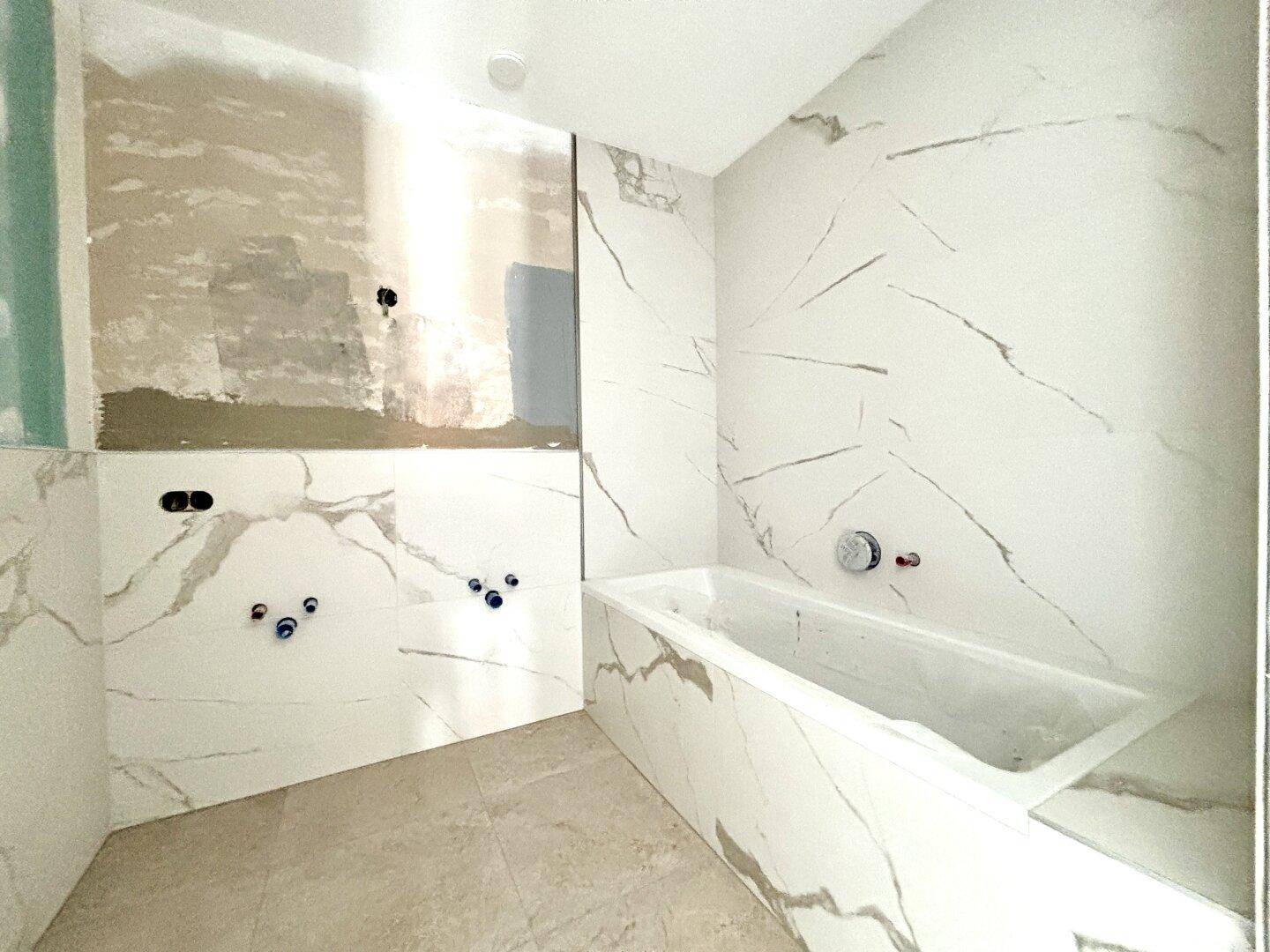 Badezimmer im Bau mit modernen Fliesen in Marmoroptik und eingebauter Badewanne.