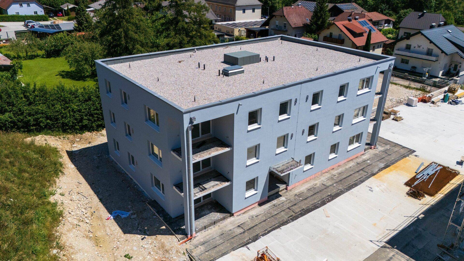 Modernes Neubaugebäude mit flachem Dach und grauer Fassade, Balkone im Bau.