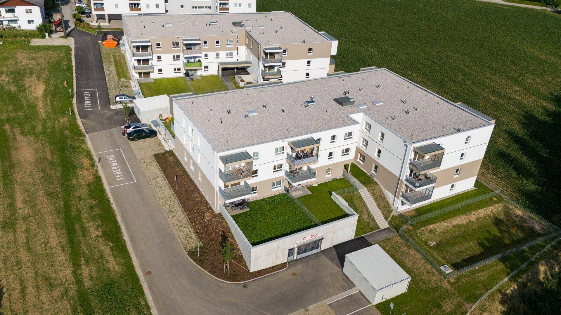 Luftaufnahme von modernen Wohngebäuden mit Flachdächern, Balkonen und begrünten Außenbereichen.