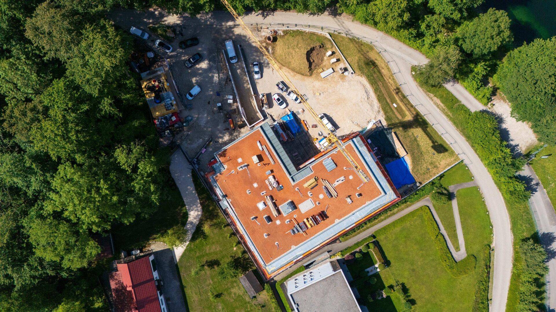 Vogelperspektive der Baustelle mit dem Flachdach des Gebäudes und der umliegenden Infrastruktur.