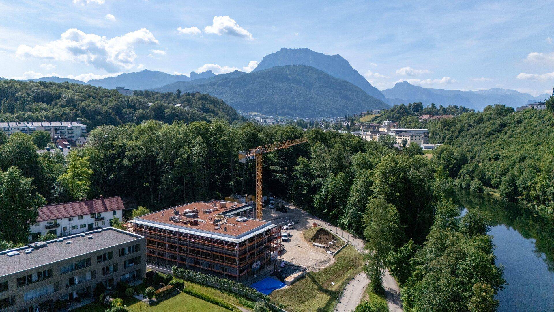 Weitläufige Luftaufnahme des Neubaus mit See und majestätischer Bergkulisse im Hintergrund.