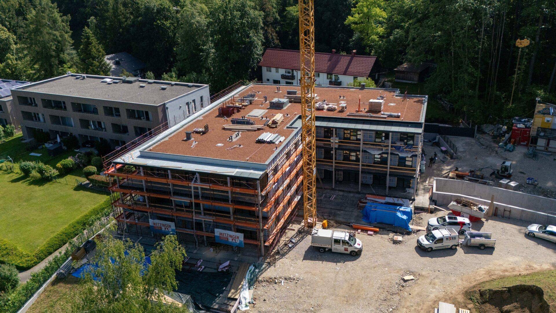 Luftaufnahme einer Baustelle mit einem im Bau befindlichen Gebäude, Kran und umliegender Natur.