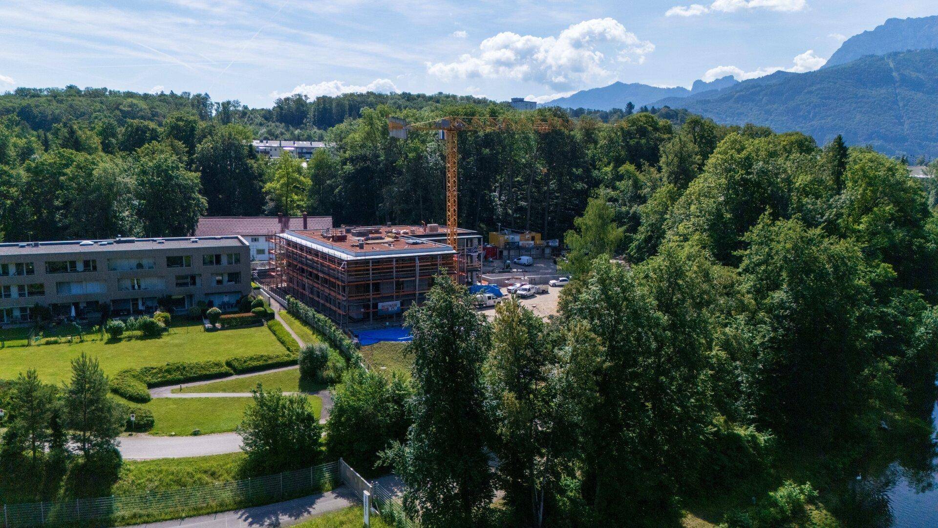 Weitläufige Luftaufnahme der Baustelle mit See, Bergen und üppiger grüner Umgebung.