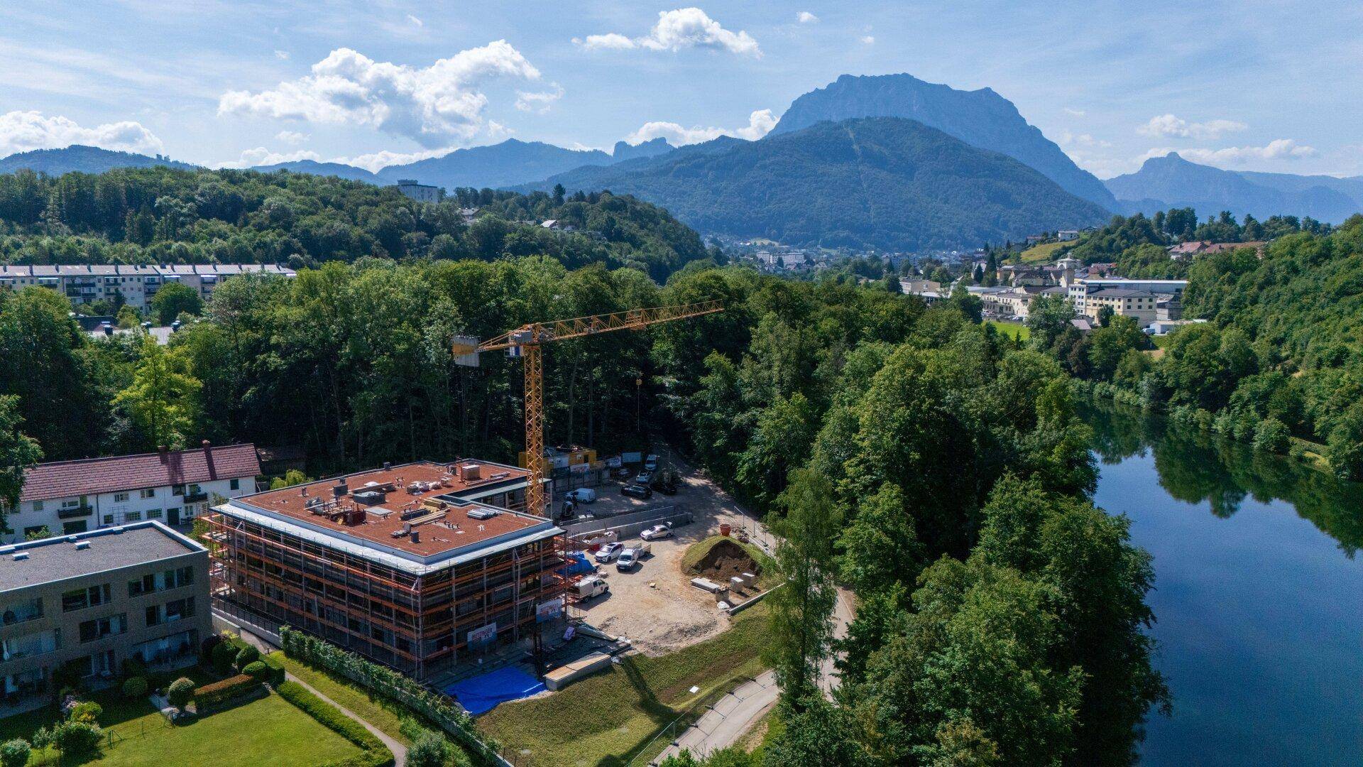 Weitläufige Luftaufnahme des Neubaus am Seeufer mit Bergblick und umliegender grüner Landschaft.