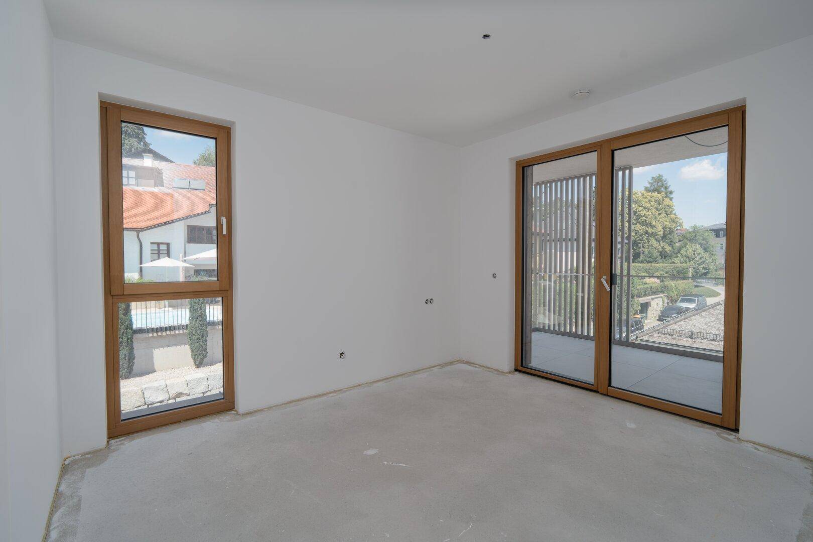 Unmöblierter Raum mit großem Fenster und Schiebetür zum Balkon, noch im Bau.