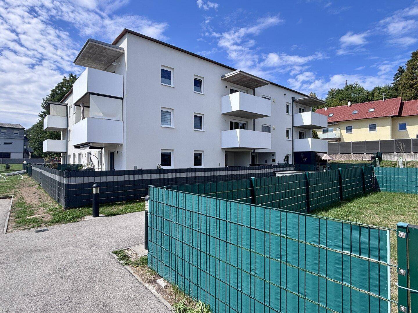 Modernes Mehrfamilienhaus mit weißen Fassaden, Balkonen und gepflegten Grünflächen.