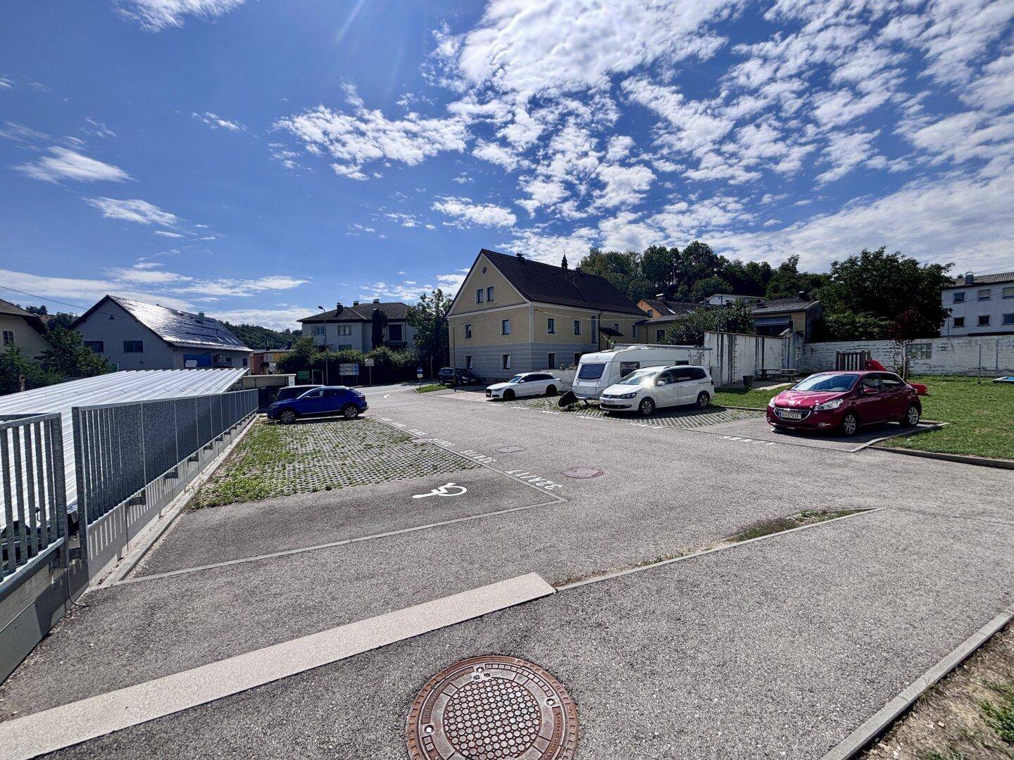 Außenparkplatz mit mehreren Fahrzeugen und einer Rampe für barrierefreien Zugang zum Gebäude.
