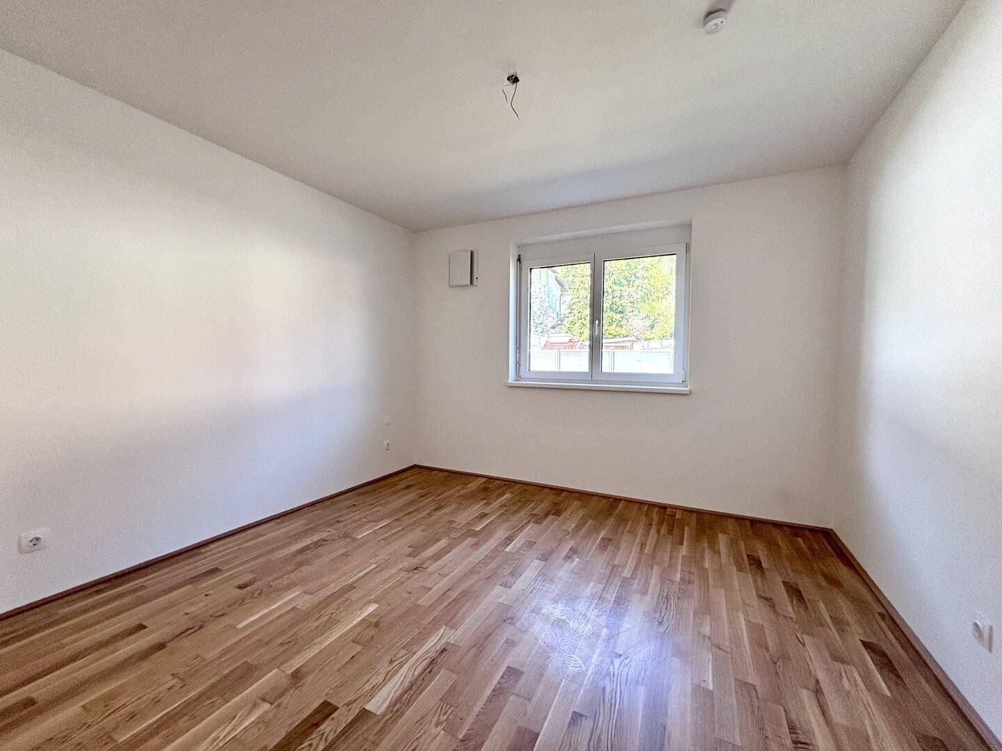 Ruhiges Schlafzimmer mit hellem Parkettboden und einem Fenster, das viel Tageslicht hereinlässt.