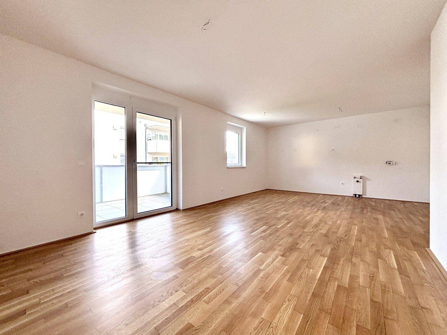 Geräumiger, heller Wohnbereich mit Parkettboden und direktem Zugang zum Balkon, bietet viel Tageslicht.