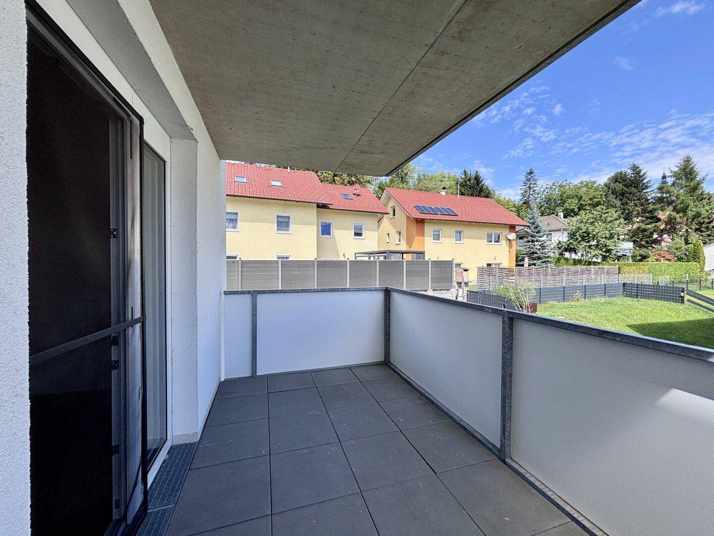 Geräumiger Balkon mit Fliesenboden und Blick auf die umliegende Wohngegend und viel Grün.