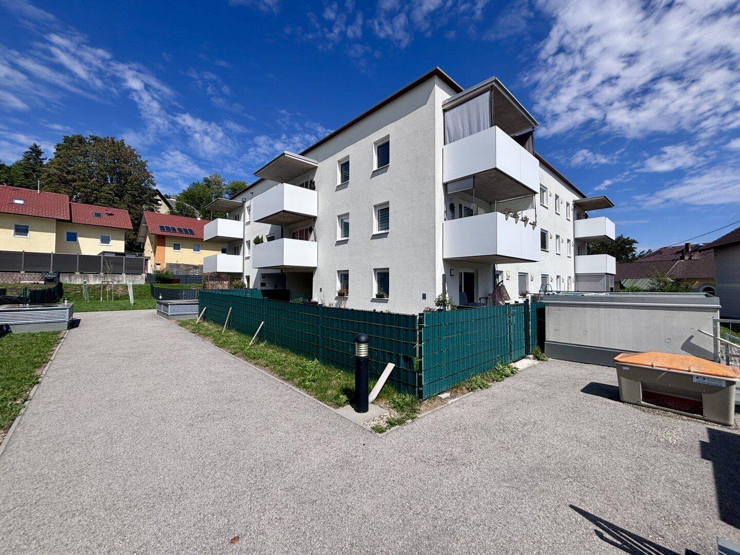 Modernes Mehrfamilienhaus mit mehreren Balkonen und gepflegten Außenanlagen unter blauem Himmel.