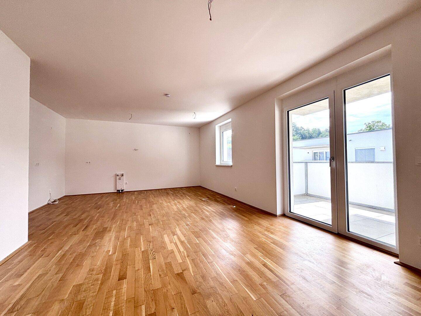 Helles, leeres Zimmer mit schönem Parkettboden und großem Zugang zu einer Terrasse.