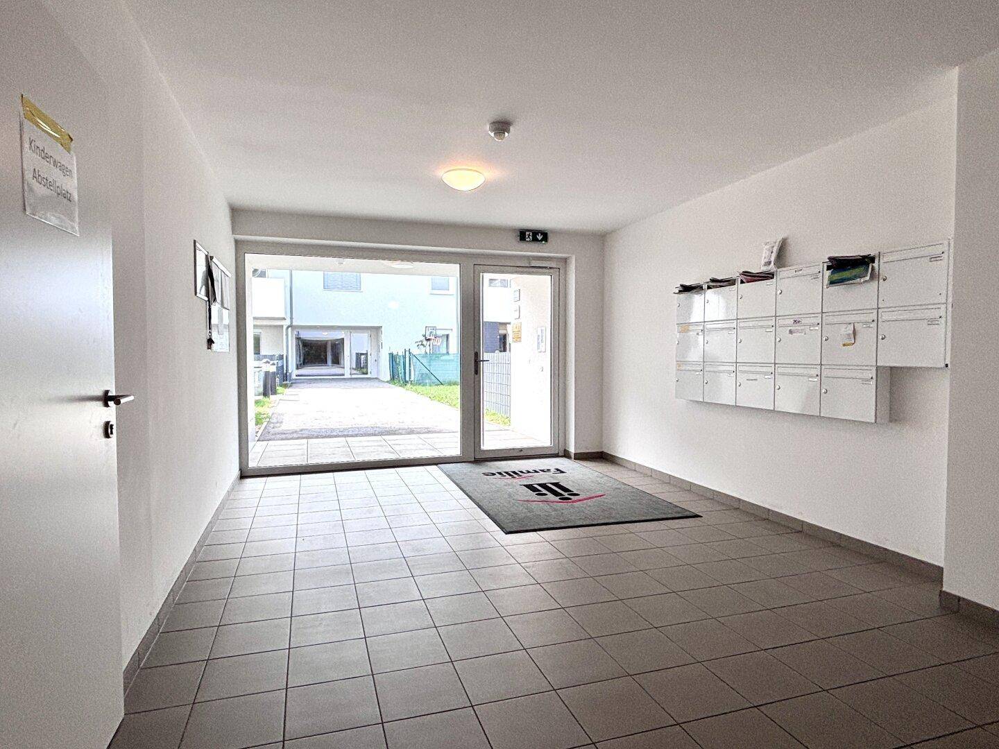 Heller Eingangsbereich eines Mehrfamilienhauses mit Briefkästen und Zugang zum Außenbereich.