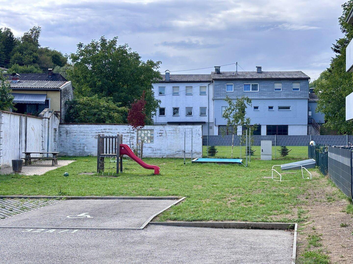 Kinderspielplatz mit Rutsche und Rasenfläche, umgeben von Wohngebäuden.