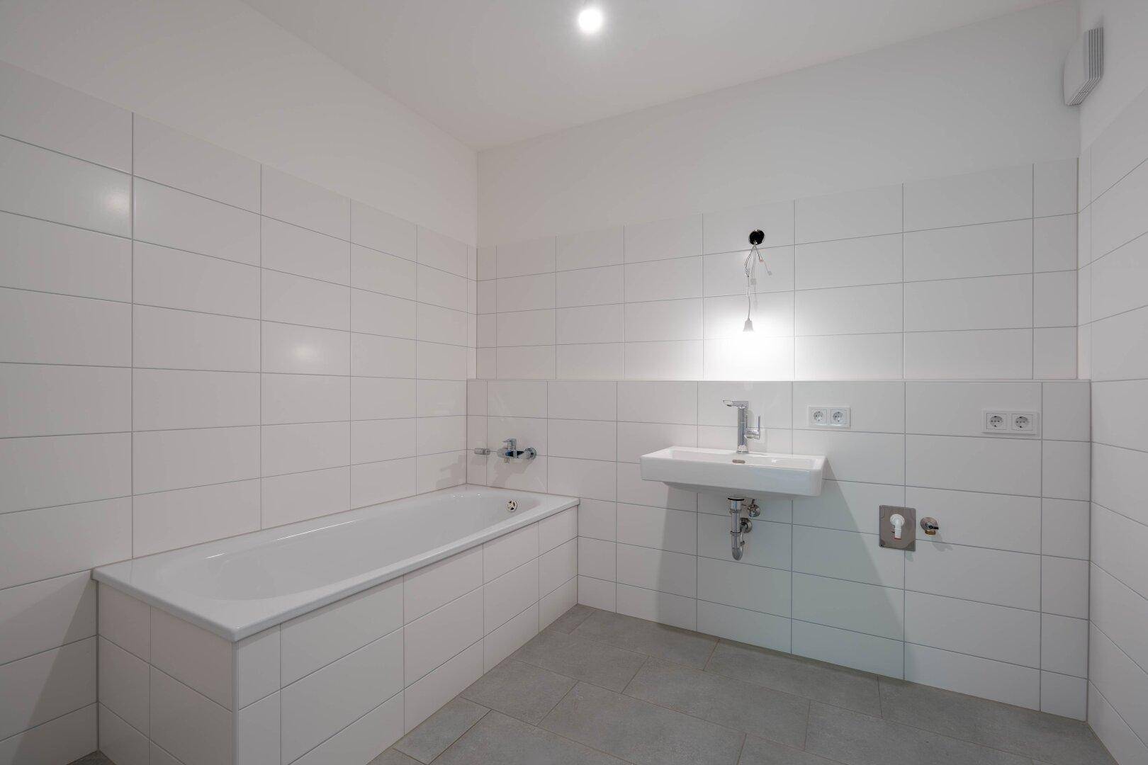 Modernes Badezimmer mit weißen Fliesen, Badewanne und Waschbecken, bereit zur Fertigstellung.